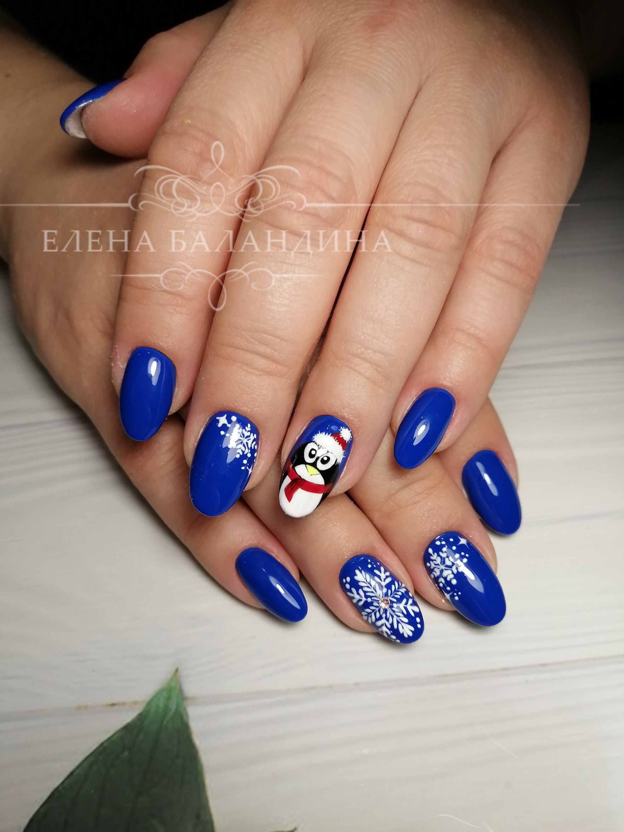 Маникюр в синем цвете с новогодним рисунком "пингвин" и "снежинки".