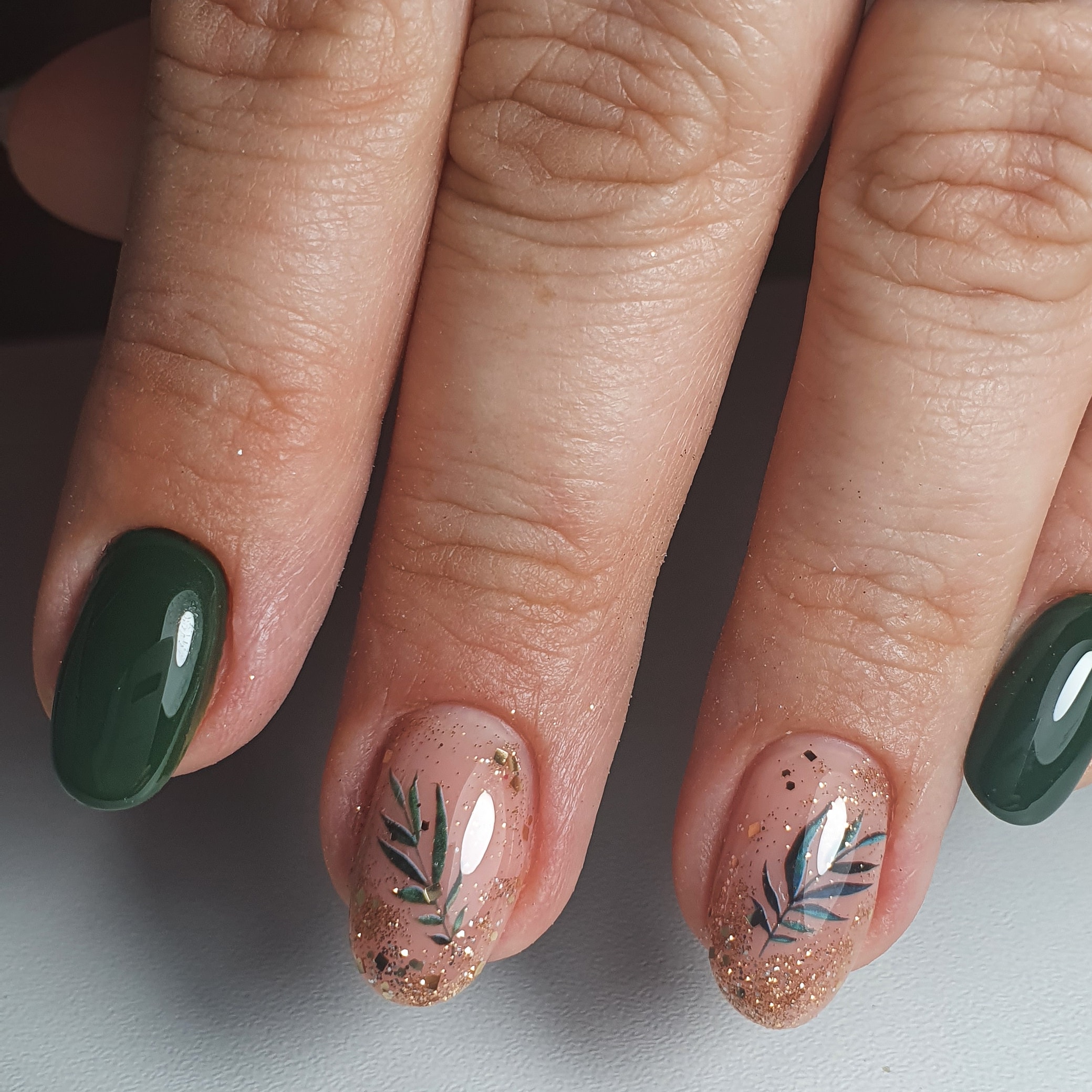 Маникюр с растительными слайдерами и золотыми блестками в темно-зеленом цвете на короткие ногти.