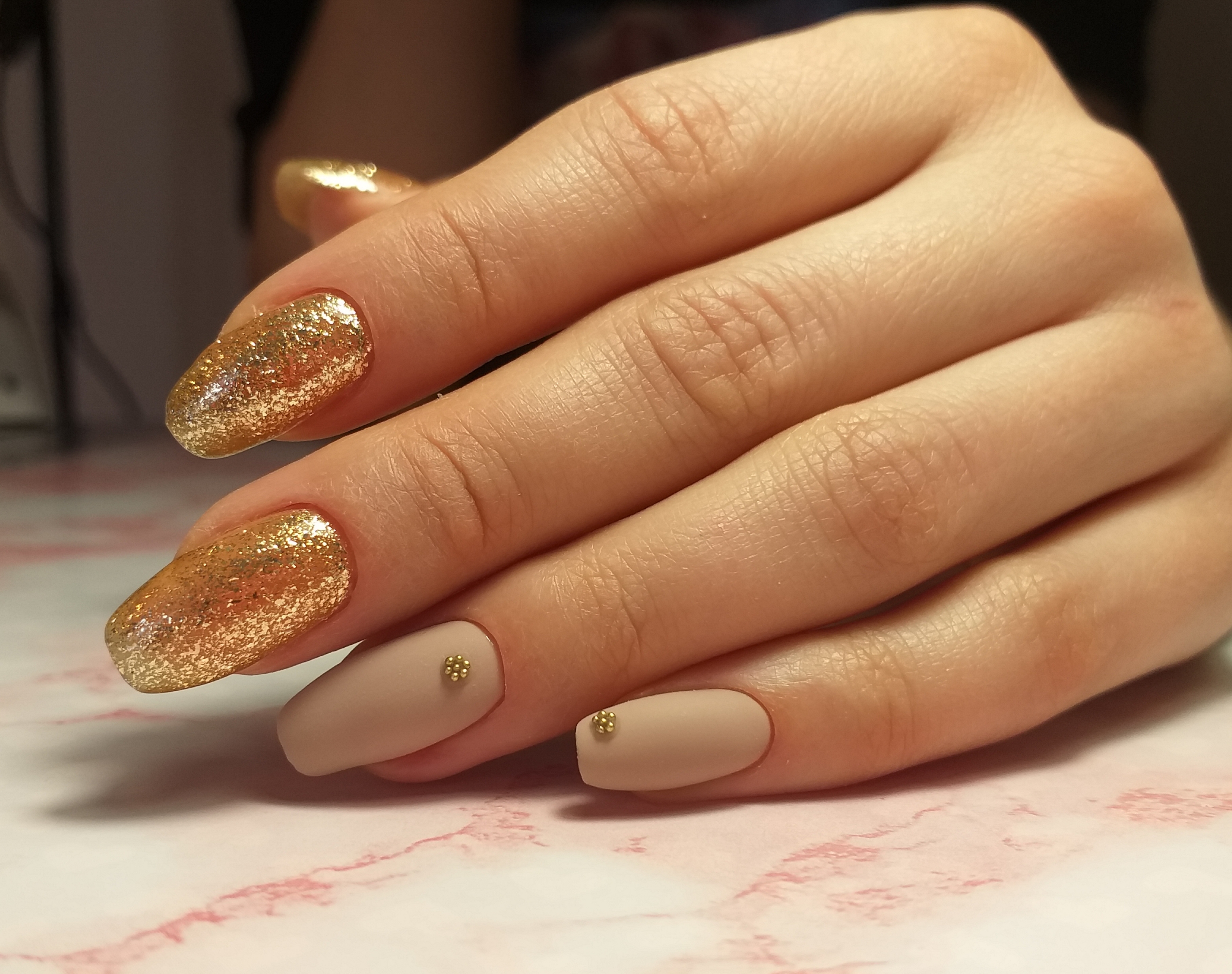 Матовый маникюр с золотыми блестками в бежевом цвете на длинные ногти.