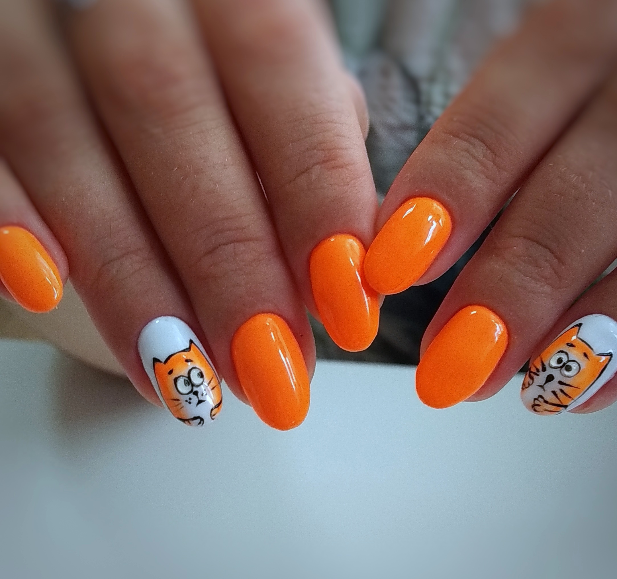 Маникюр в оранжевом цвете с белым дизайном и мультяшным рисунком "котики".