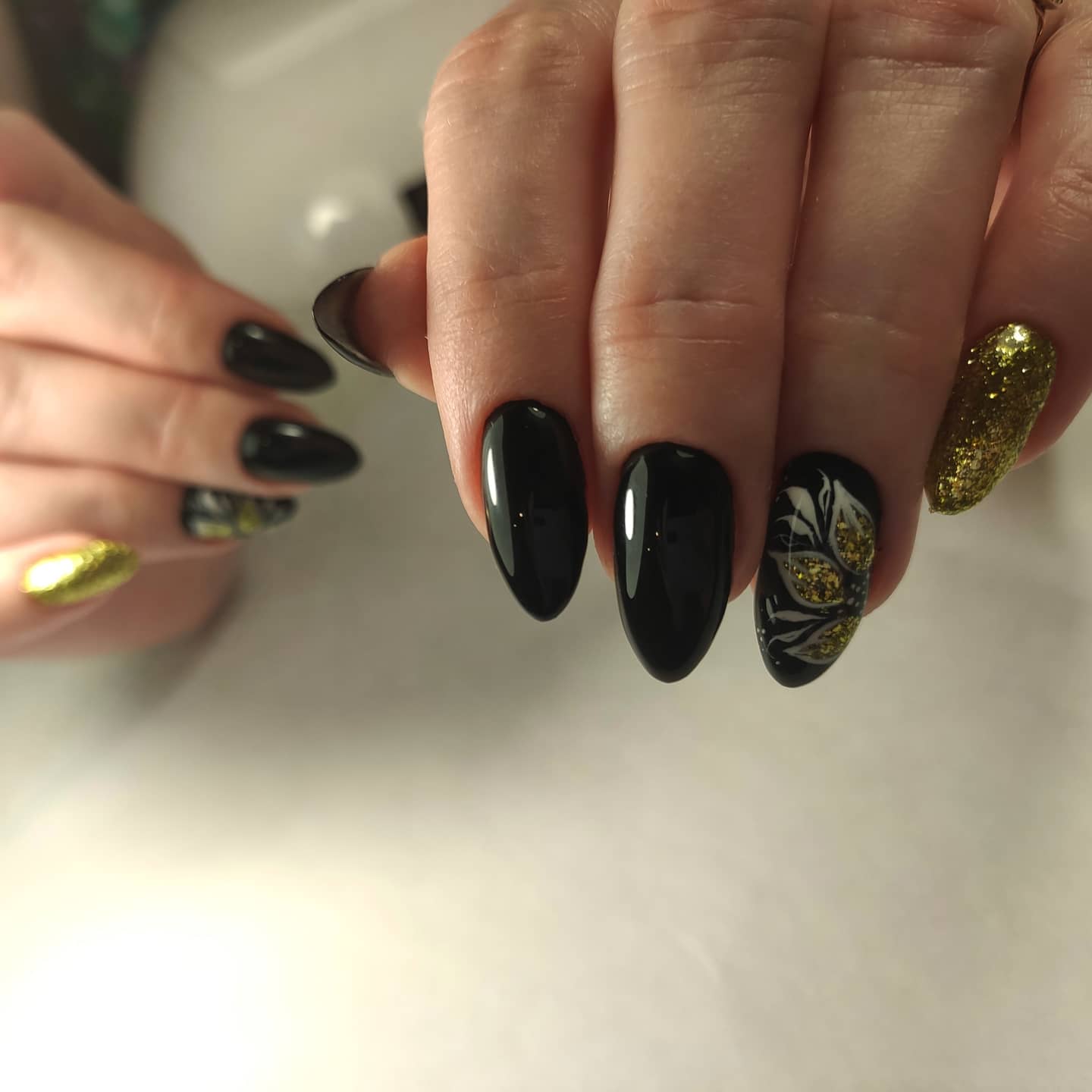 Маникюр с цветочным рисунком и золотыми блестками в черном цвете на длинные ногти.